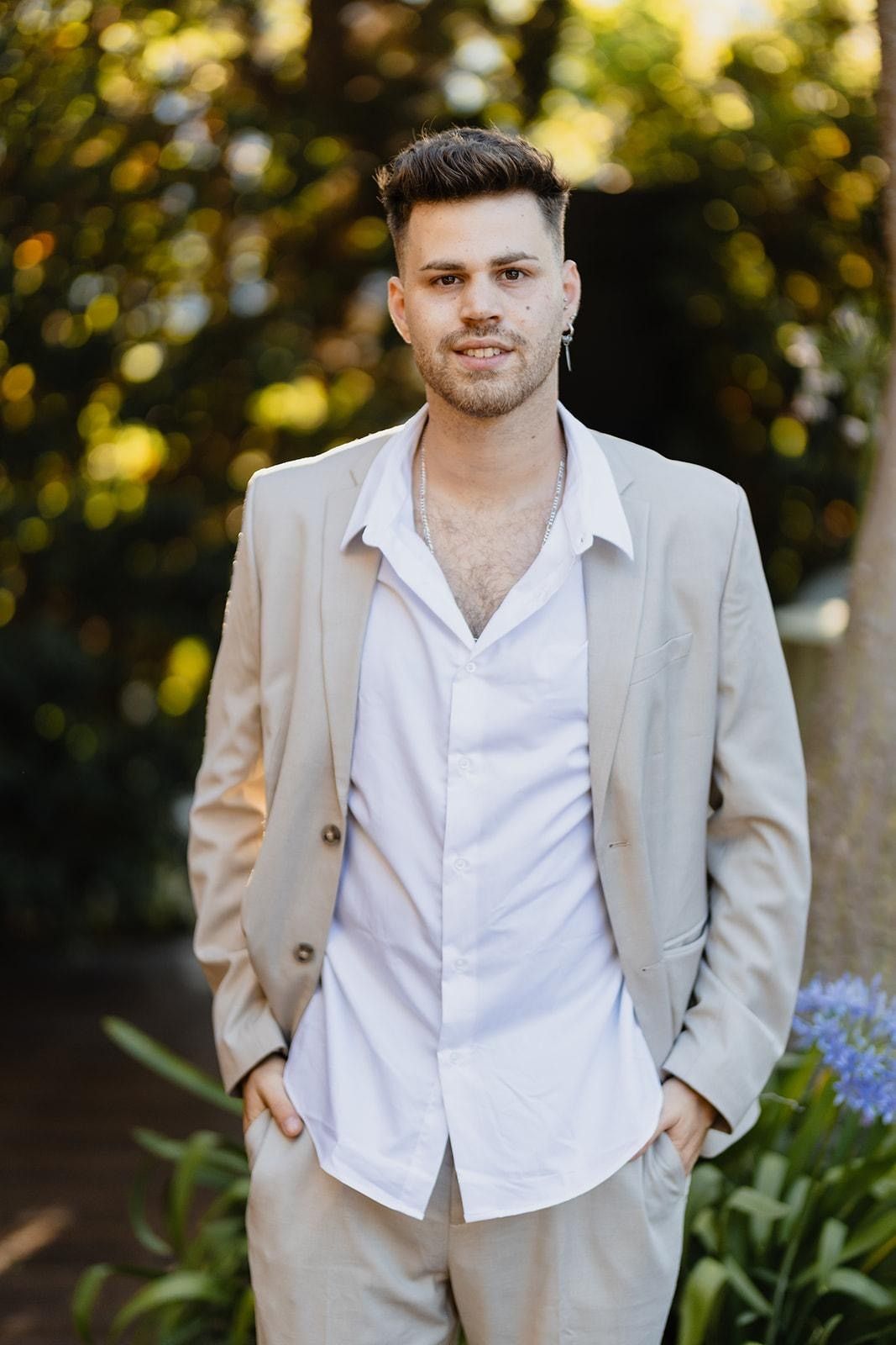 Portrait of Roni Michaeli in a light suit, smiling, in a sunlit garden